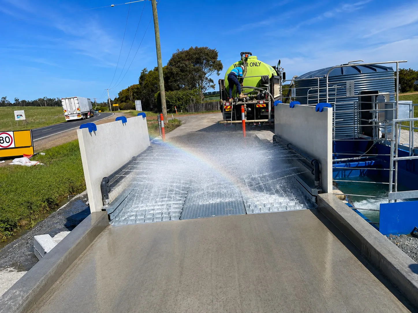 Truck driving through a wash ramp beside its water recycle tank