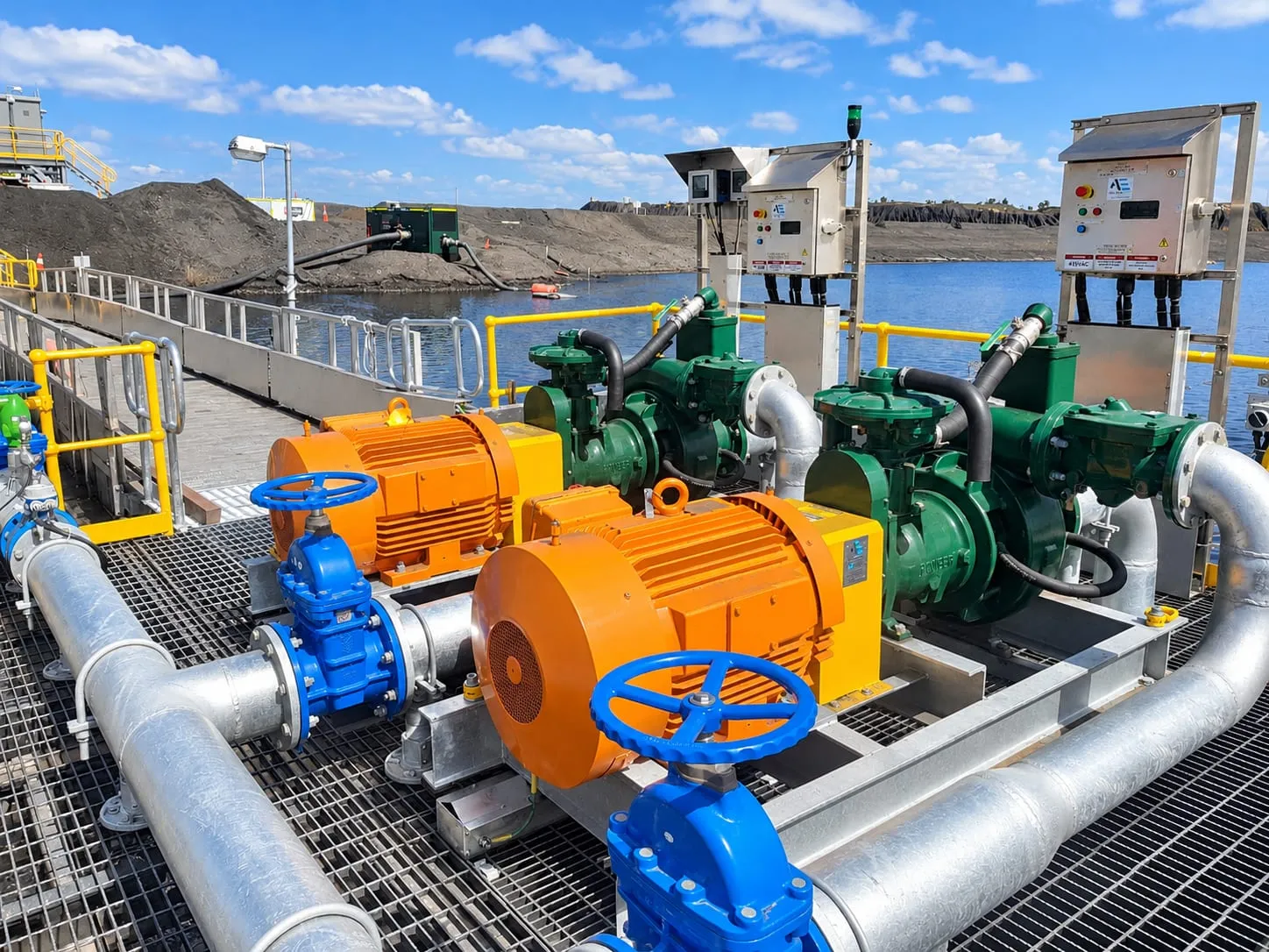 Twin electric dewatering pump sets with orange motors and control panels on a platform beside a mine water storage