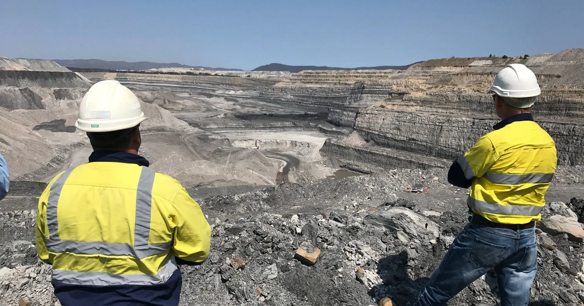 Two engineers in hi-vis overlooking an open-cut mine