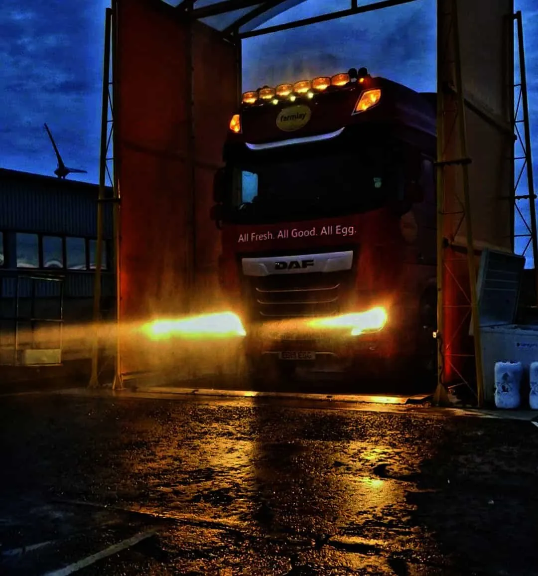 Truck passing through a vehicle disinfection gate with spray arches at night