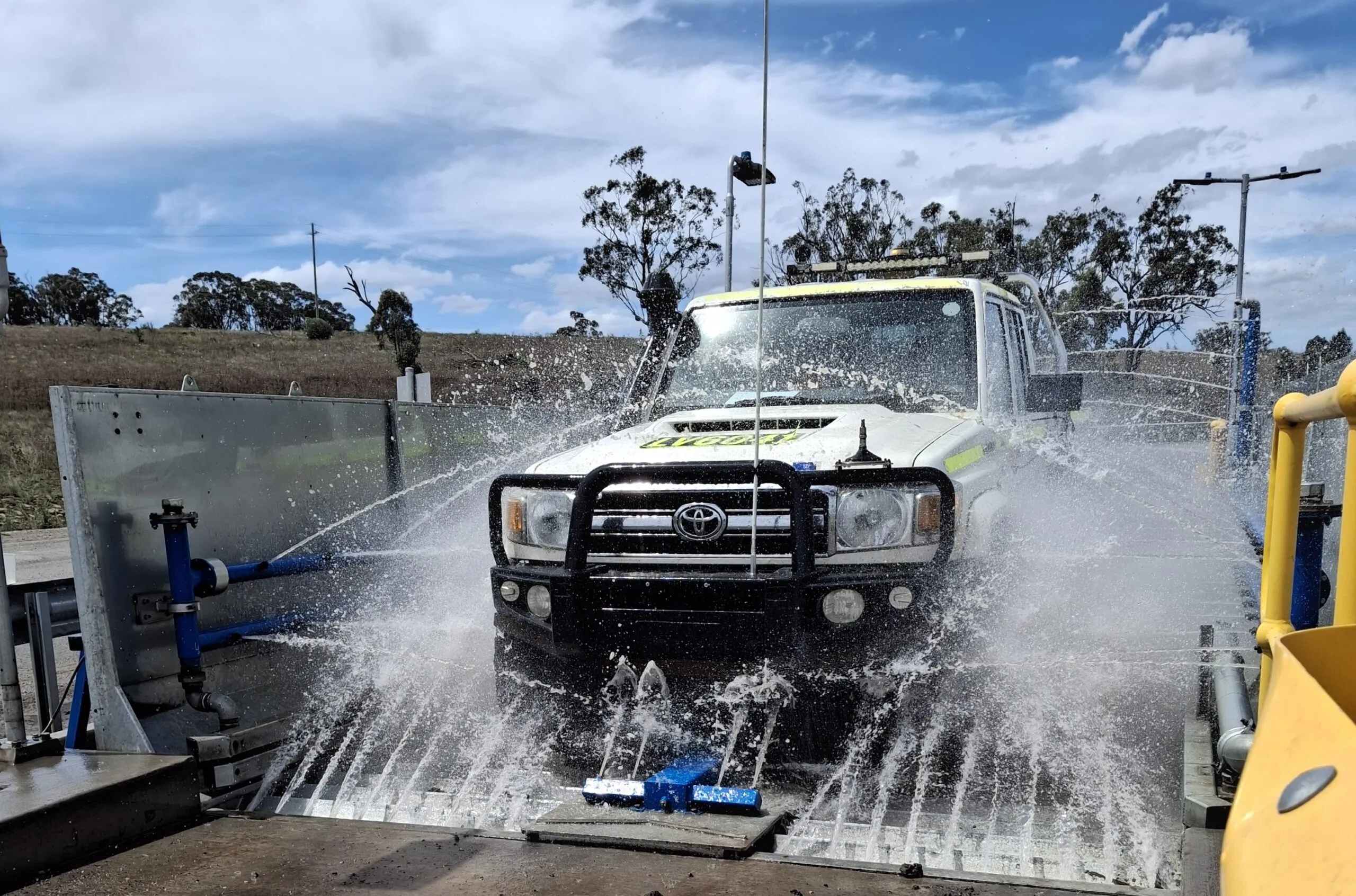 Four-wheel drive passing through a drive-through wash bay under high-pressure wheel and chassis wash jets