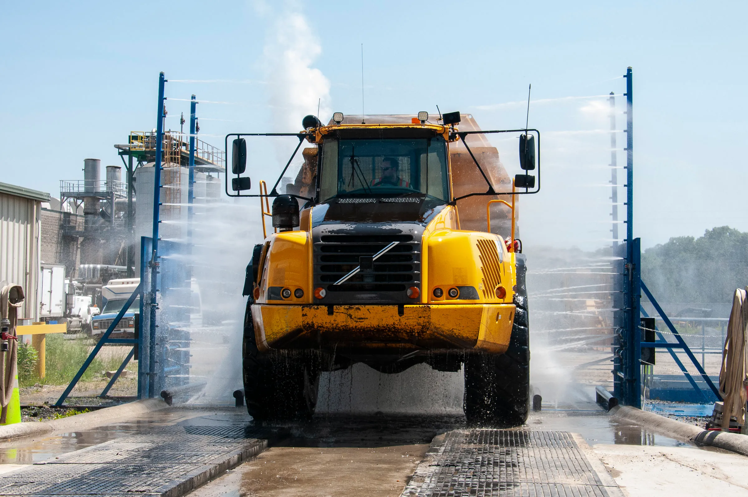 Articulated dump truck driving through a drive-through wash with spray bars on both sides