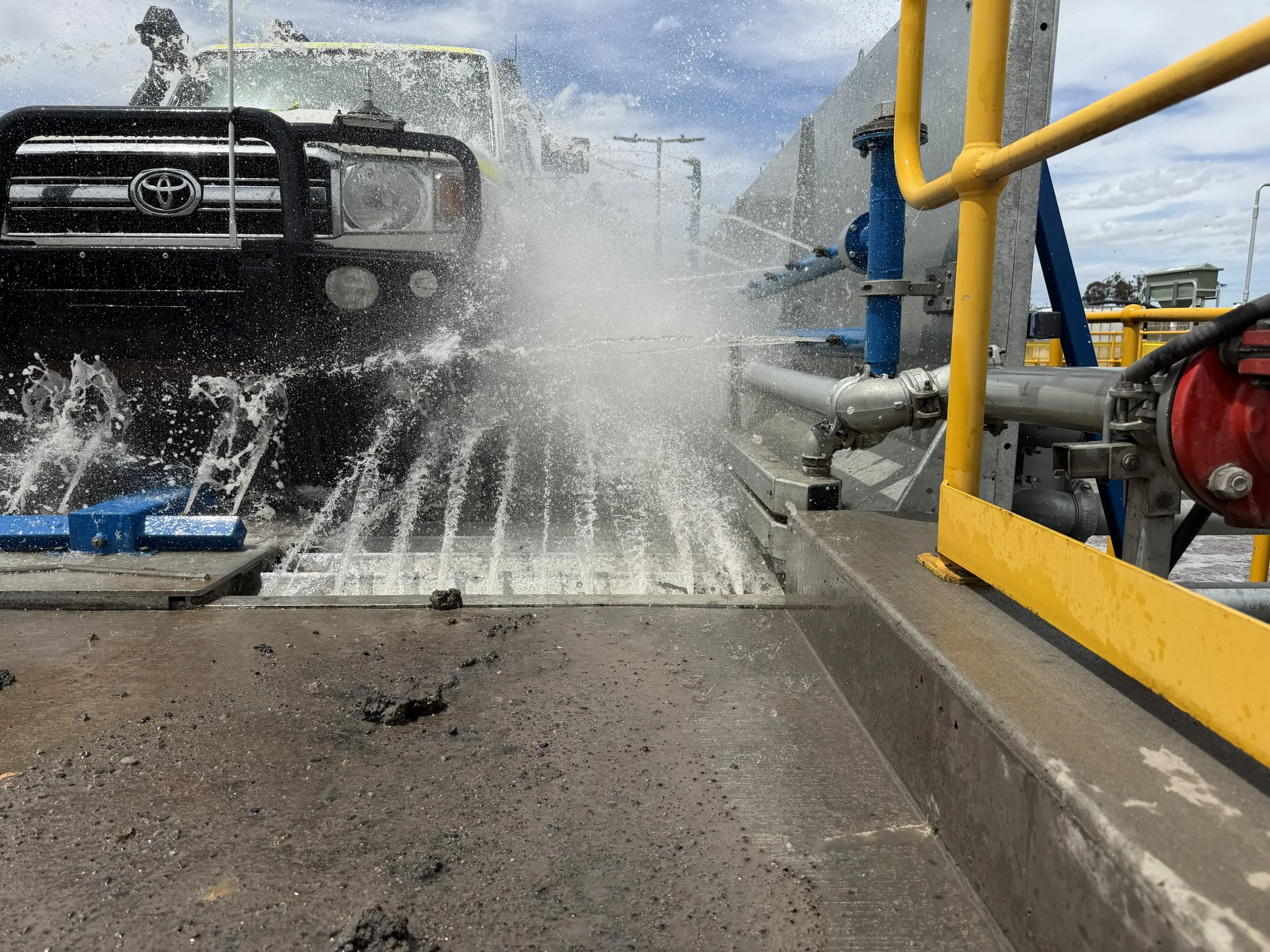 Four-wheel drive passing through a wheel and undercarriage wash, water jets spraying from the floor