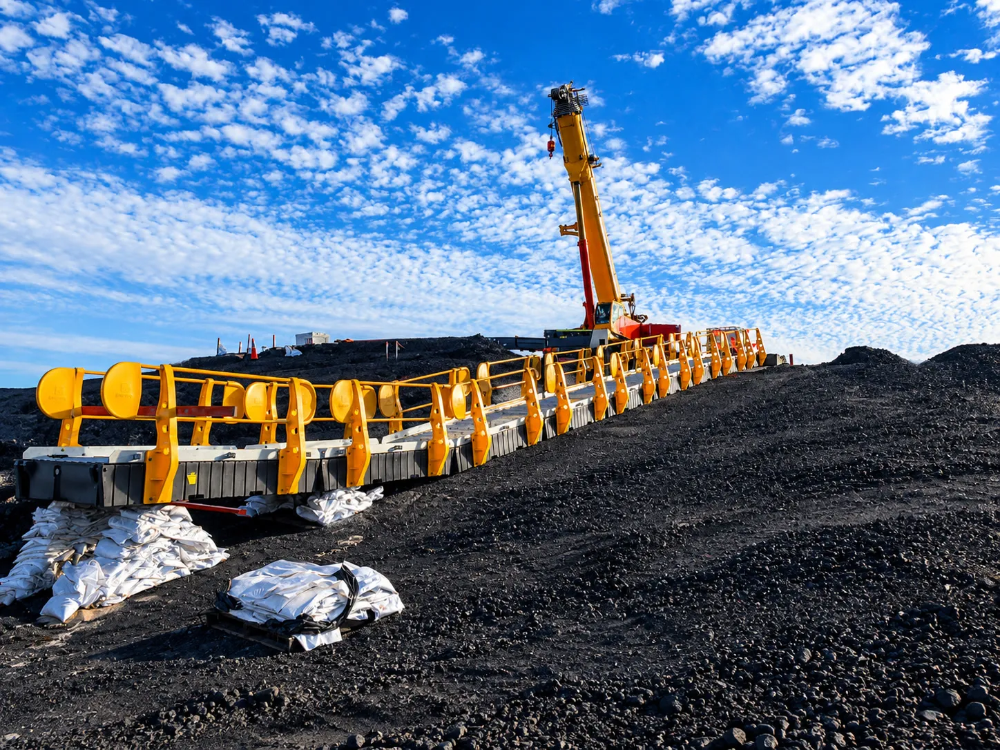 Floating walkway with yellow handrails being installed by crane on a mine site