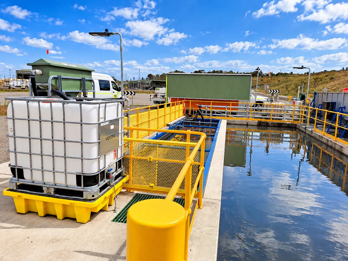 Wash water settling pit with safety railings and a chemical dosing tote